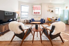 A modern living room with a flat-screen TV, a sofa, two armchairs, a coffee table, and a dining area with chairs.