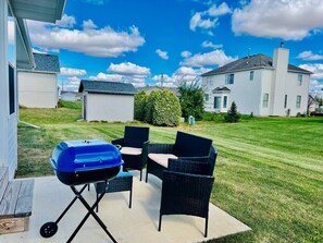 Een terras met een barbecue, tuinmeubilair en een verzorgd gazon.