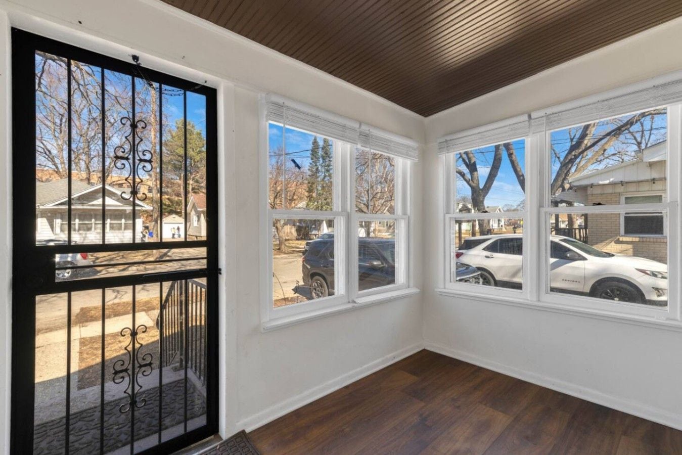 A room with a wooden ceiling, a black gate, and three windows with blinds.