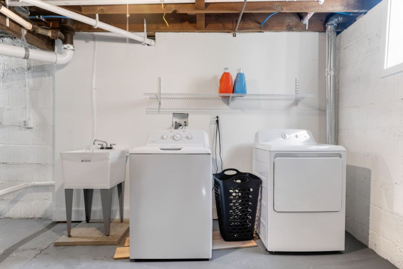 A laundry room with two washing machines, a sink, and a shelf with bottles.
