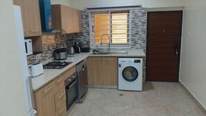 A compact kitchen with a washing machine, a microwave, and a stove. - A Perfect Home for the Family 3 Bed , (Accra Hills)