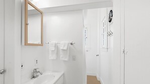 Un baño blanco con lavamanos, espejo y perchero.