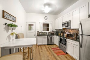 A modern kitchen with white cabinets, stainless steel appliances, a dining table with chairs, and a clock on the wall.