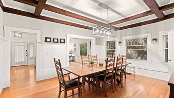 A spacious dining area with a wooden table and chairs, a hanging light fixture, and a view through a window with a lattice design.