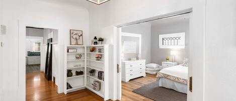 Un intérieur moderne avec un plancher en bois, des murs blancs, une bibliothèque intégrée, une commode blanche et un lit agrémenté d’un tapis gris.