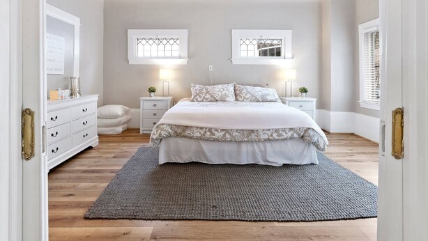 Un dormitorio con cama, mesitas de noche, ventilador de techo y dos ventanas con contraventanas.