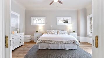 A bedroom with a bed, bedside tables, a ceiling fan, and two windows with shutters.