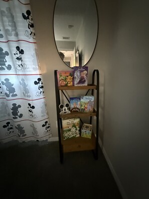 A shelf with books and a mirror in a room with a Mickey Mouse curtain. - Villa Bella Sol, 5BR, Sleeps 14, Pool/ Spa, Disney (Davenport)
