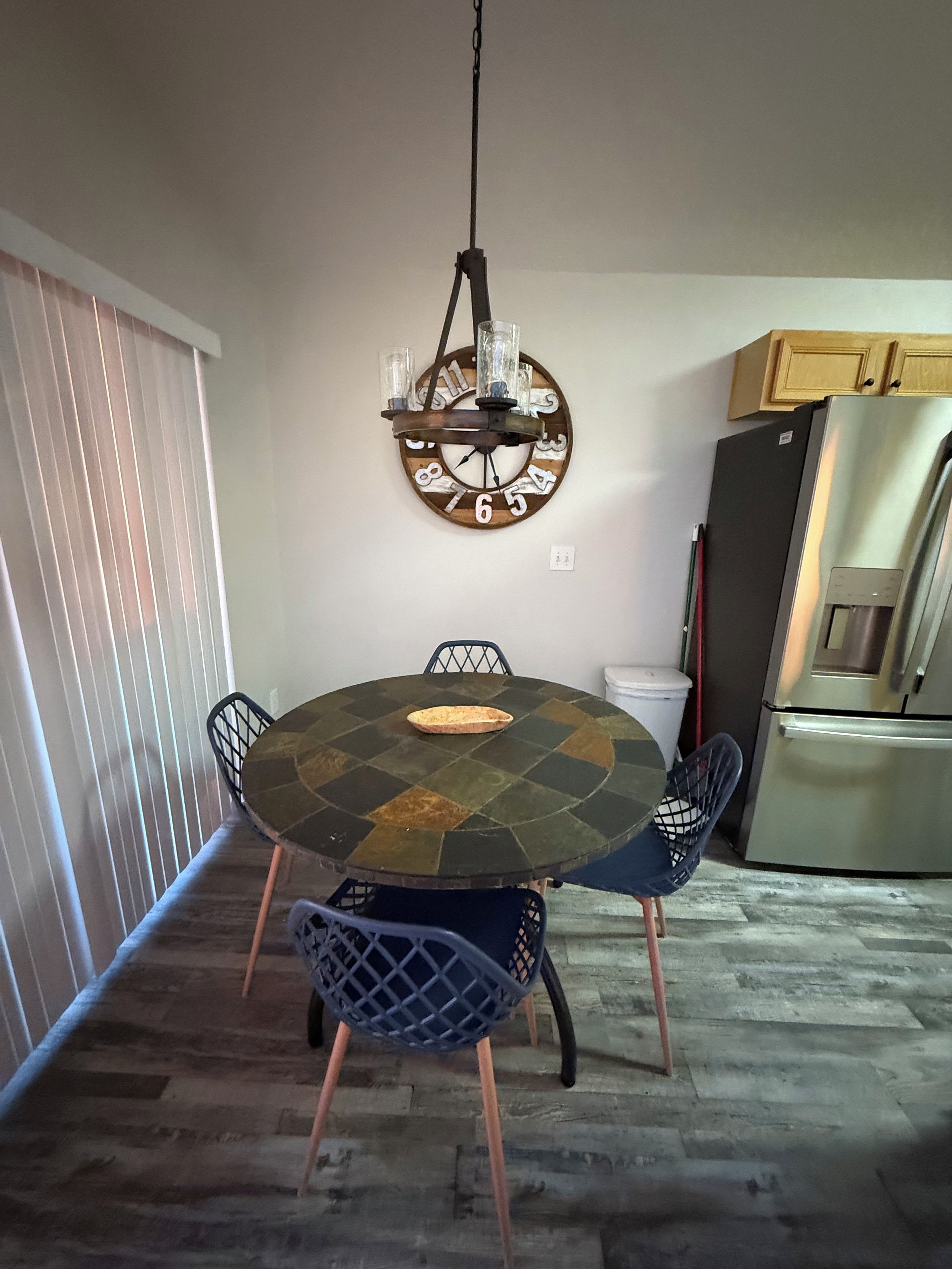 Un coin repas comprenant une table ronde, des chaises, une horloge murale et un réfrigérateur.