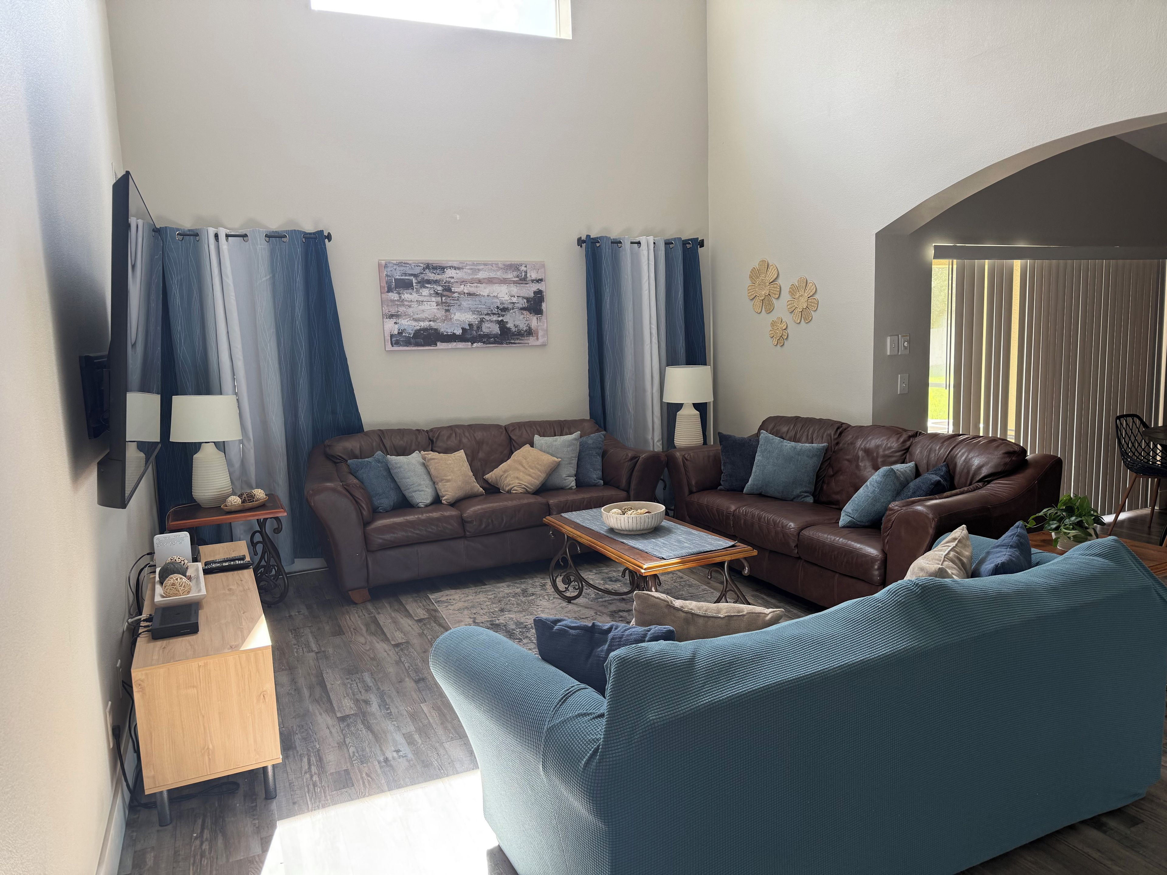 Un salon avec un canapé en cuir marron, un fauteuil bleu, une table basse en bois et un téléviseur fixé au mur.