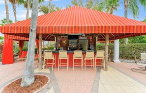 A covered outdoor bar area with a red-striped roof, multiple bar stools, and a counter. - Villa Bella Sol, 5BR, Sleeps 14, Pool/ Spa, Disney (Davenport)
