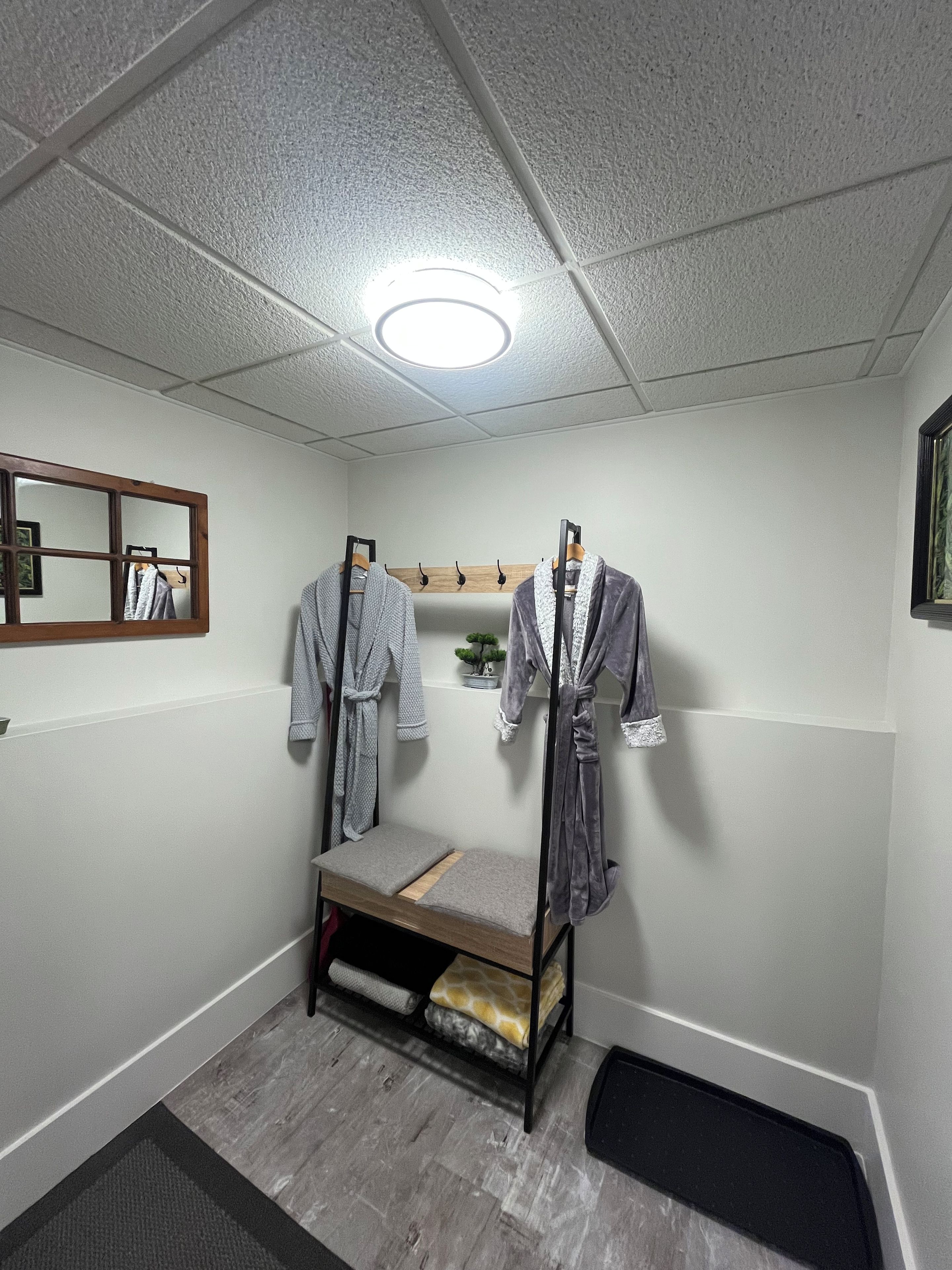 Une petite chambre privée avec un lit superposé, une étagère en bois où sont rangés des peignoirs, une petite plante et un miroir au mur.