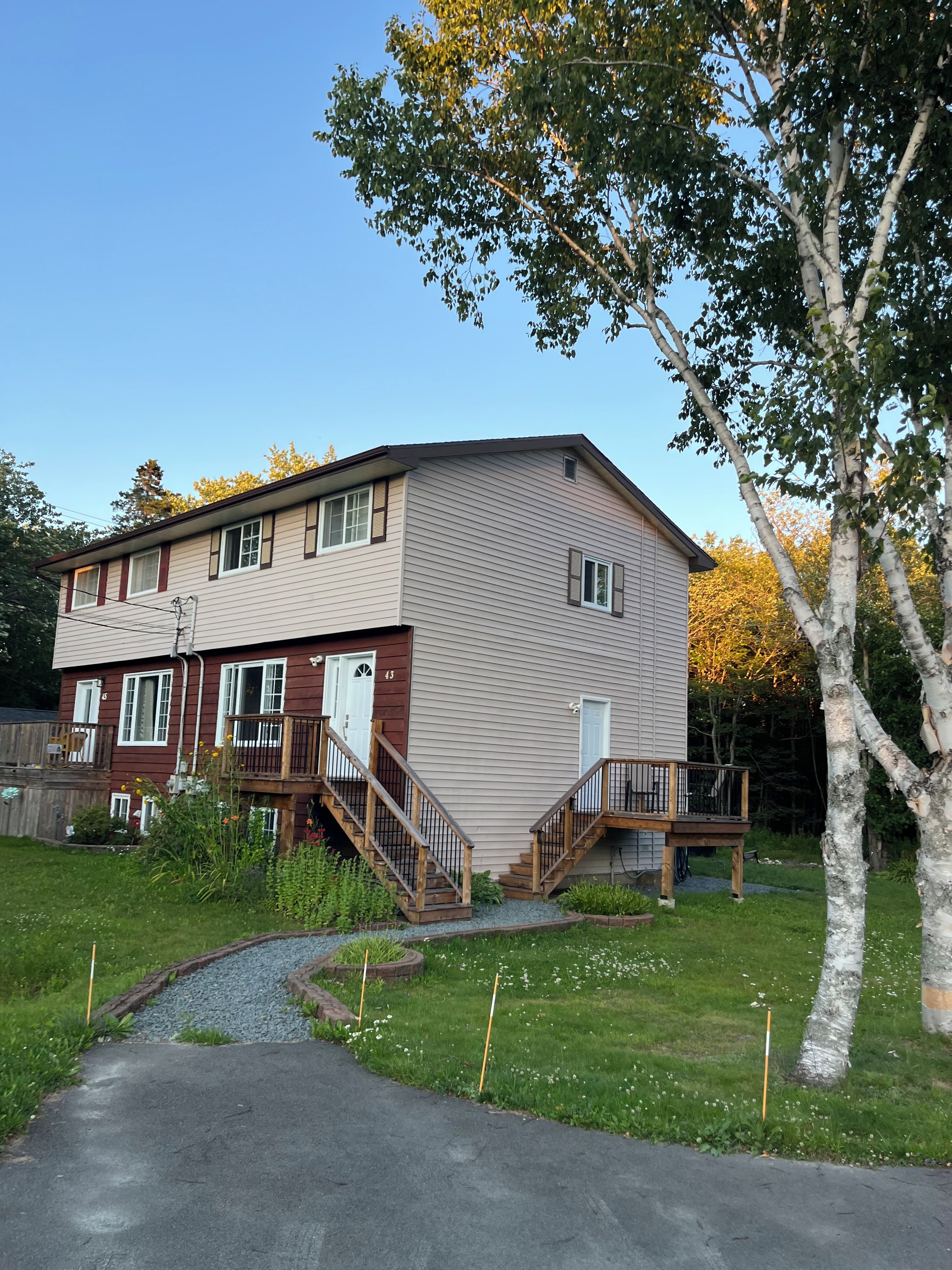 A two-story residential building with a front deck, a small front yard, and a tree.