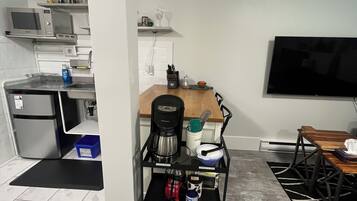 A compact living space with a kitchenette, a coffee machine, a TV, and a dining area.