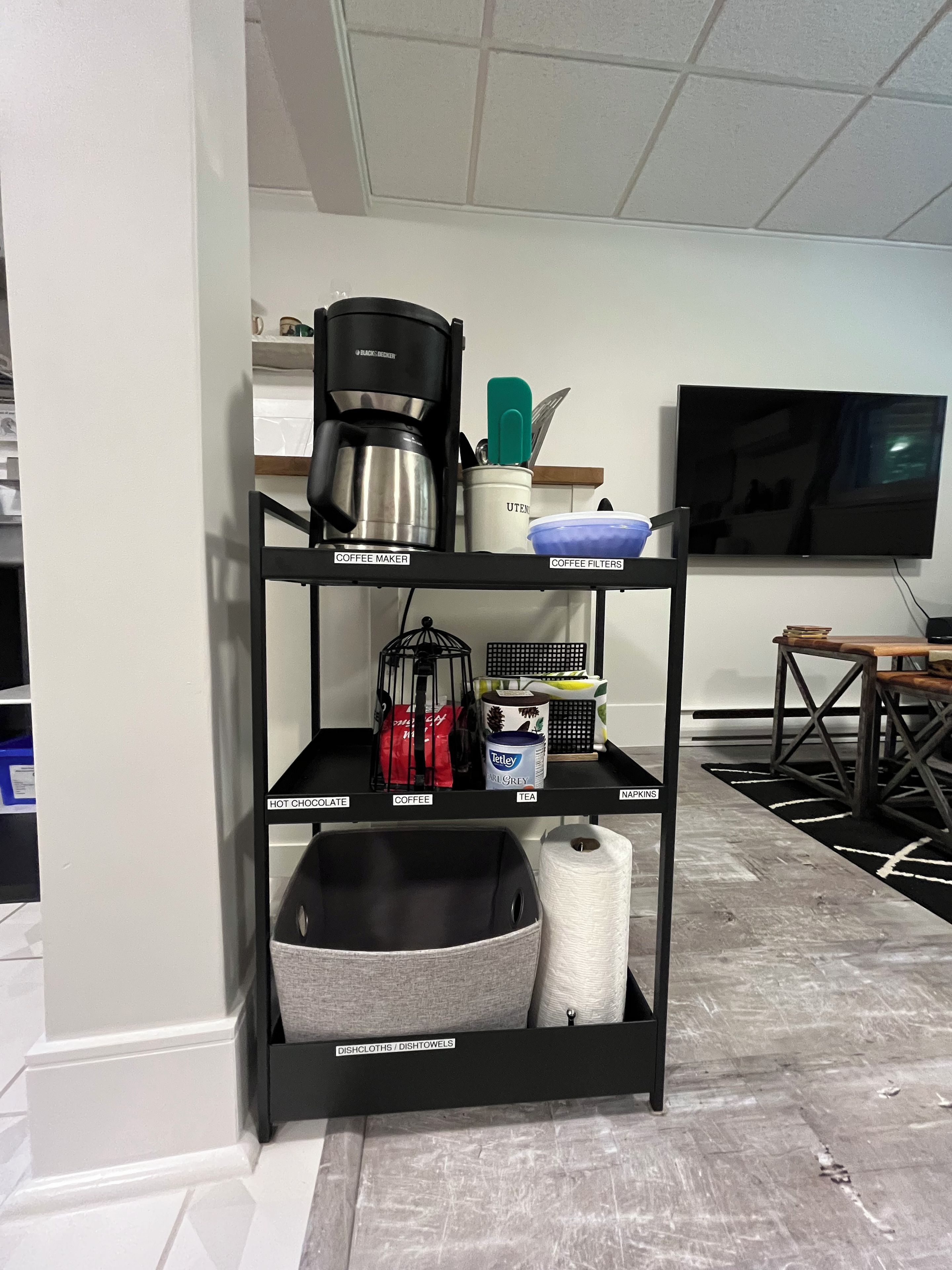 A kitchen area with a coffee maker, tea, and hot chocolate on the shelves.
