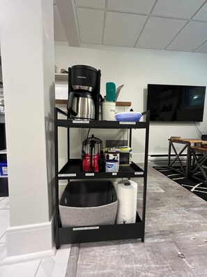 A kitchen area with a coffee maker, tea, and hot chocolate on the shelves.
