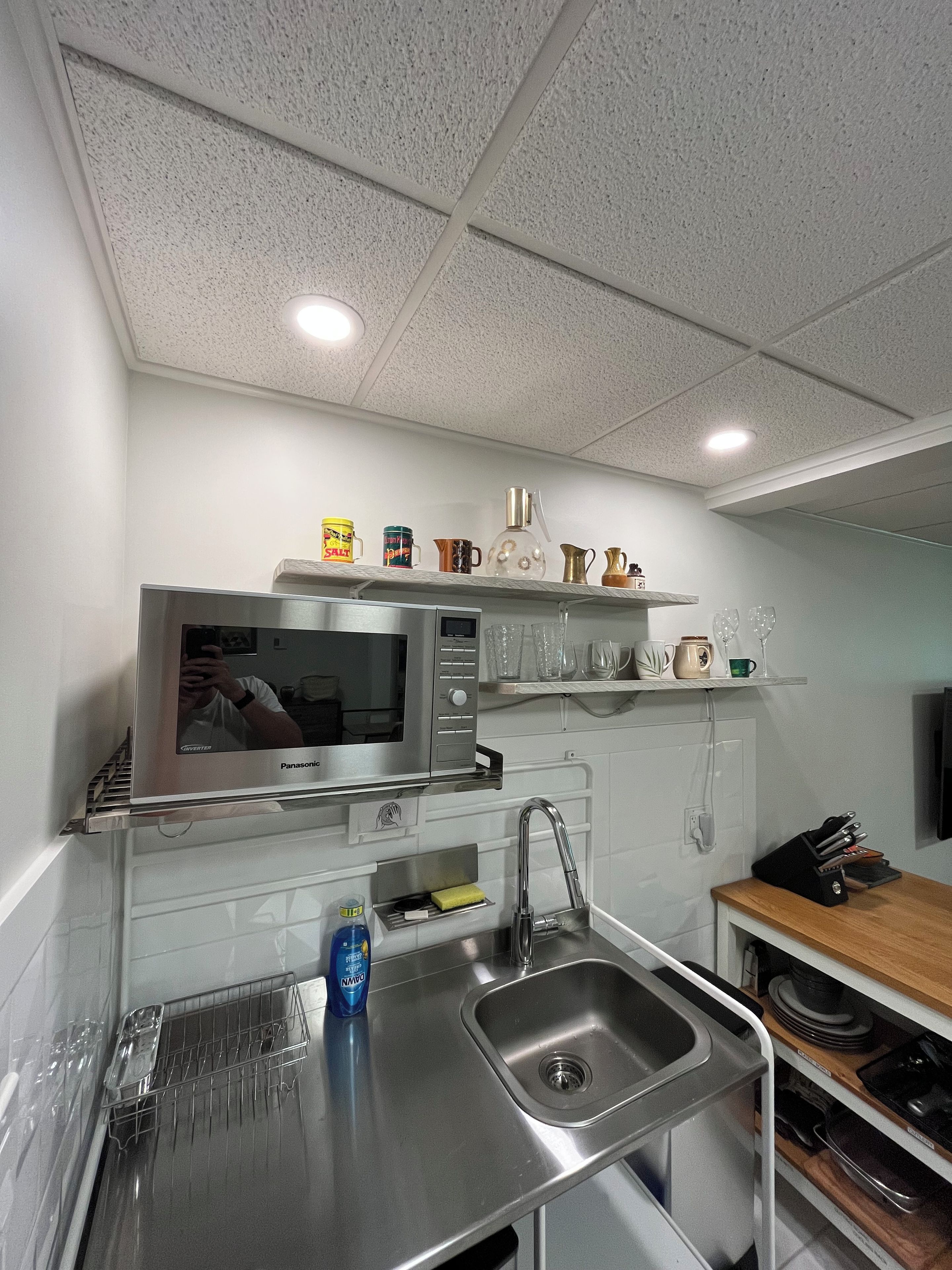 Una cucina con un lavandino in acciaio inossidabile, un forno a microonde e uno scaffale con diversi utensili da cucina.