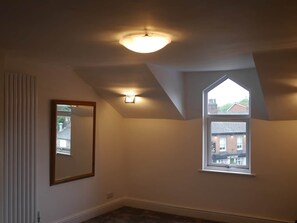 A room with a sloped ceiling, a single window, and a mirror on the wall. - Didsbury Village Apartment (Manchester)