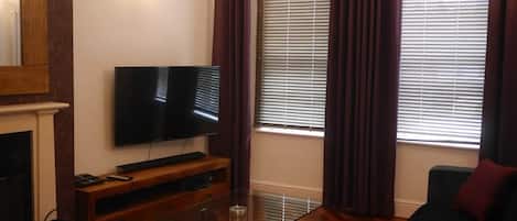 Un soggiorno con una TV a schermo piatto su un supporto in legno, un tavolino da caffè in vetro, un divano e un camino.