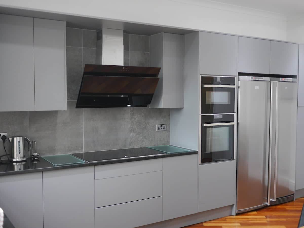 A modern kitchen with grey cabinets, a stainless steel refrigerator, and a built-in oven.