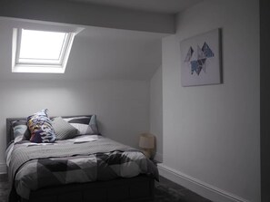 A bedroom with a bed, a pillow, a bedside lamp, a wall-mounted artwork, and a skylight. - Didsbury Village Apartment (Manchester)