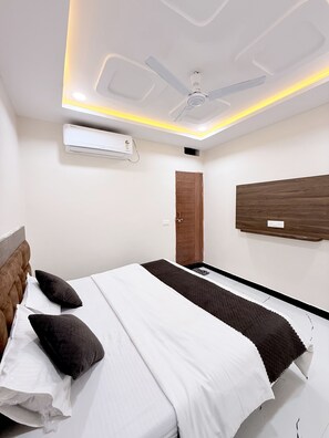 Une chambre à coucher moderne avec un lit, des oreillers, un ventilateur de plafond, un appareil de climatisation et un mur d’accent en bois.