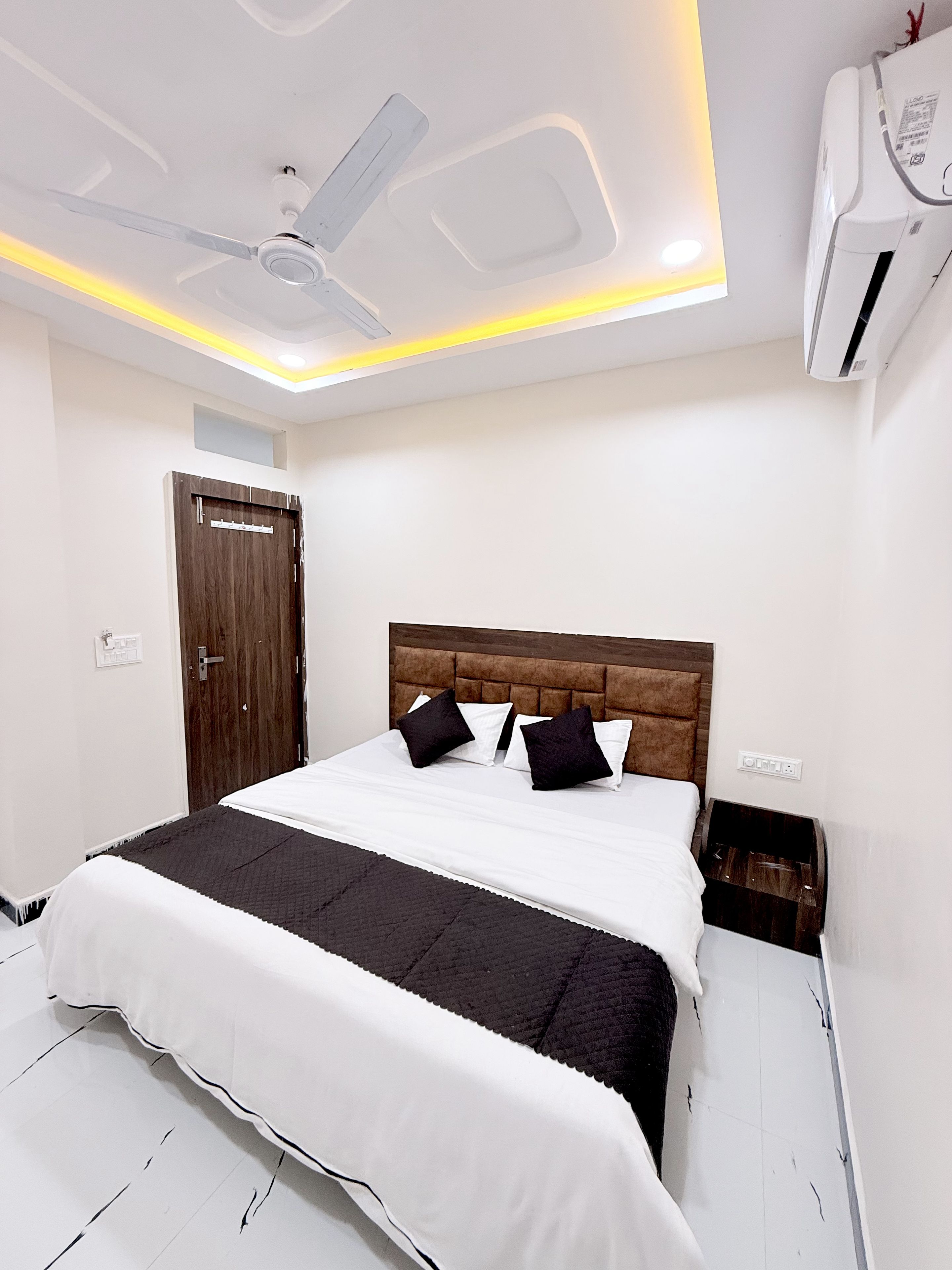 Un dormitorio con cama, ventilador de techo, aire acondicionado y una puerta.