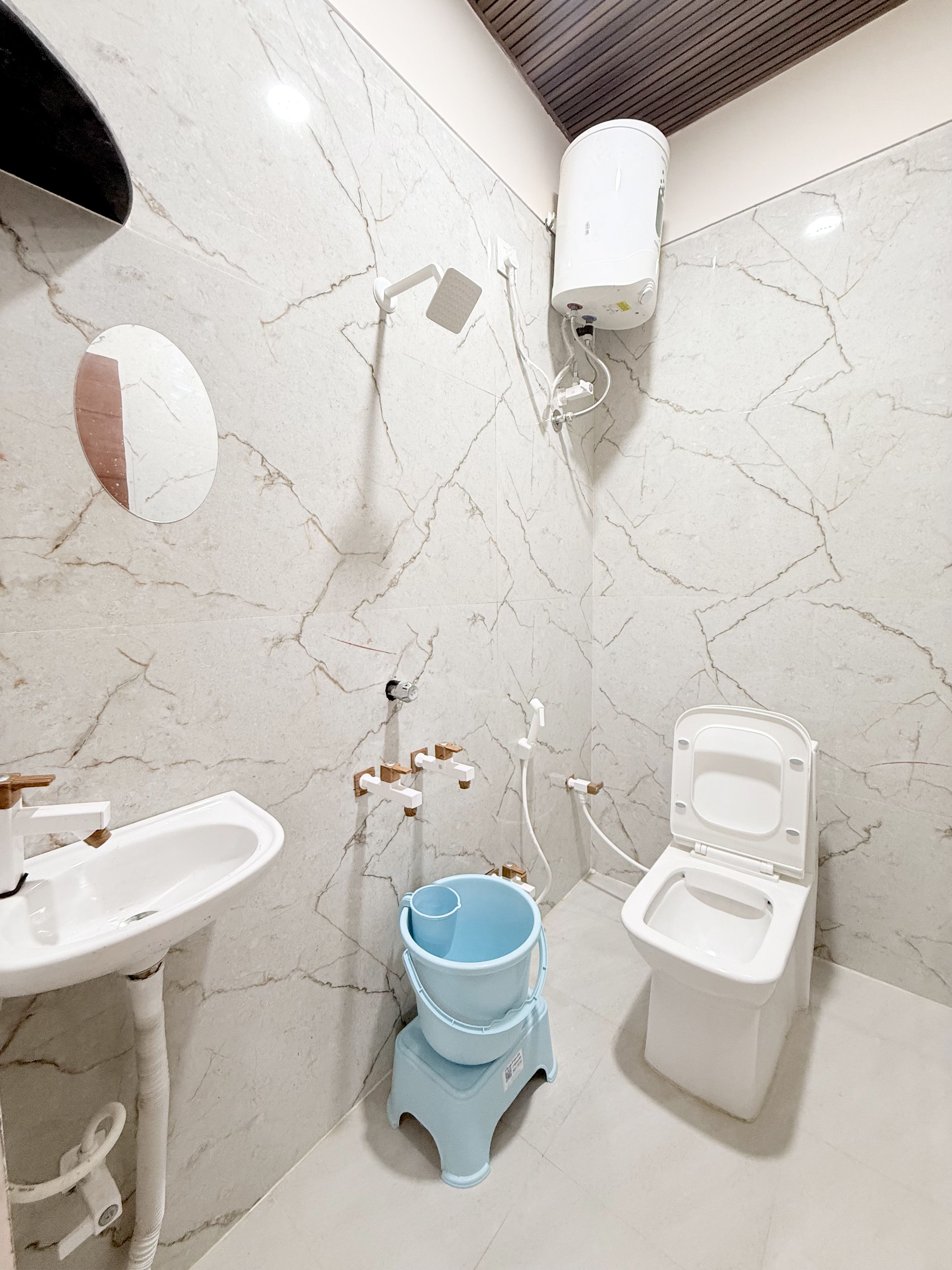 Un baño con lavamanos, inodoro y bidé blancos, paredes de mármol y un techo con paneles de madera.