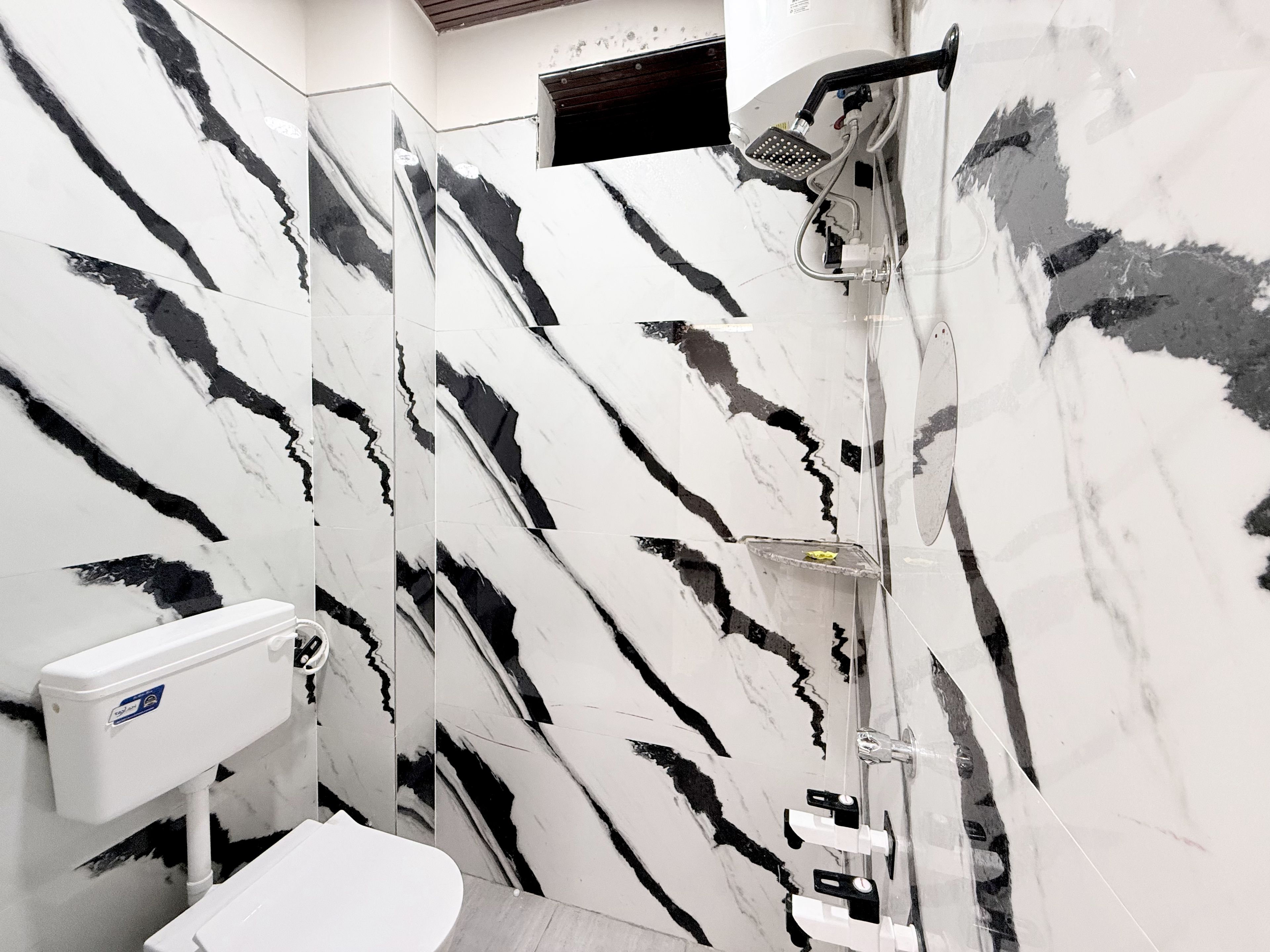 A bathroom with a marble wall, a shower, and a toilet.
