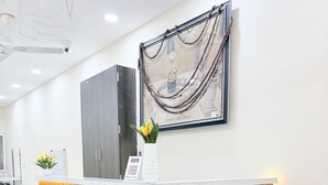 A reception area with a wooden reception desk, a blue sofa, and a framed artwork on the wall. - Hotel Vaishnavi Mahakal (UJJAIN)
