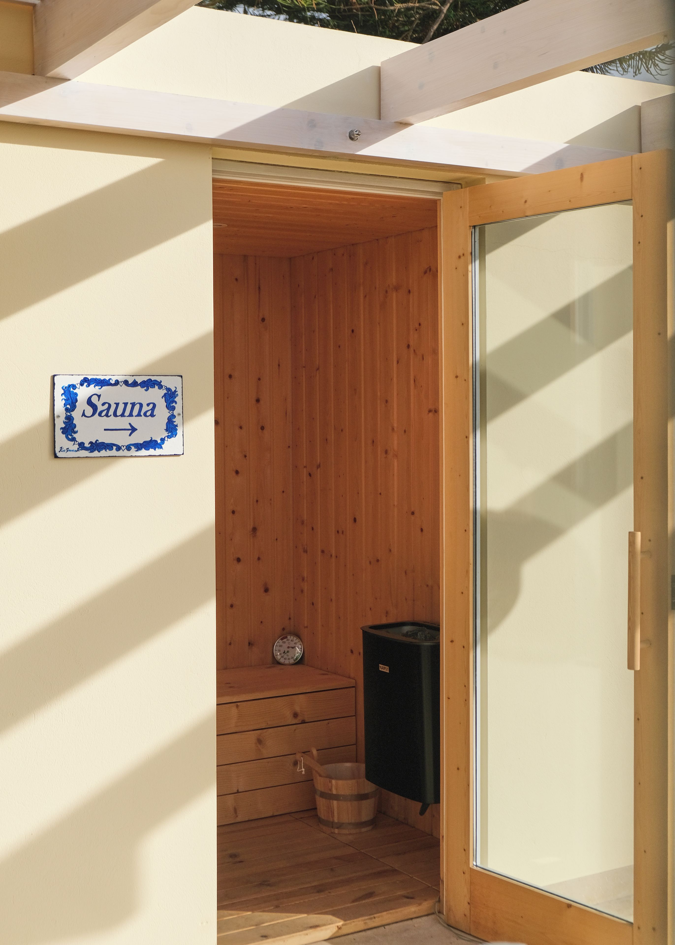 Una sauna con pareti in legno, un cartello che ne indica la funzione, una panca in legno e un termostufa per sauna.