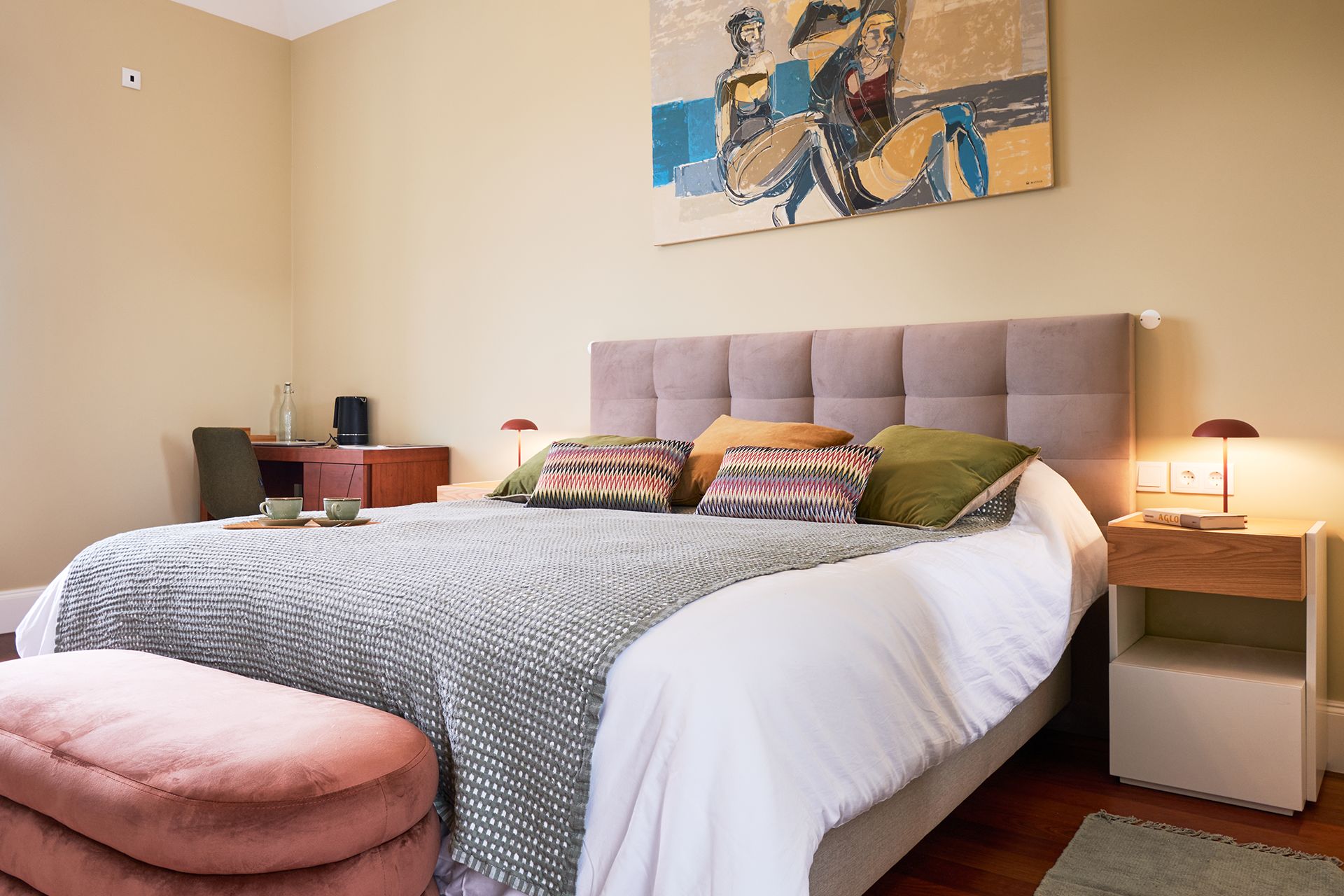 A bedroom with a bed, a nightstand, a lamp, and a painting on the wall.