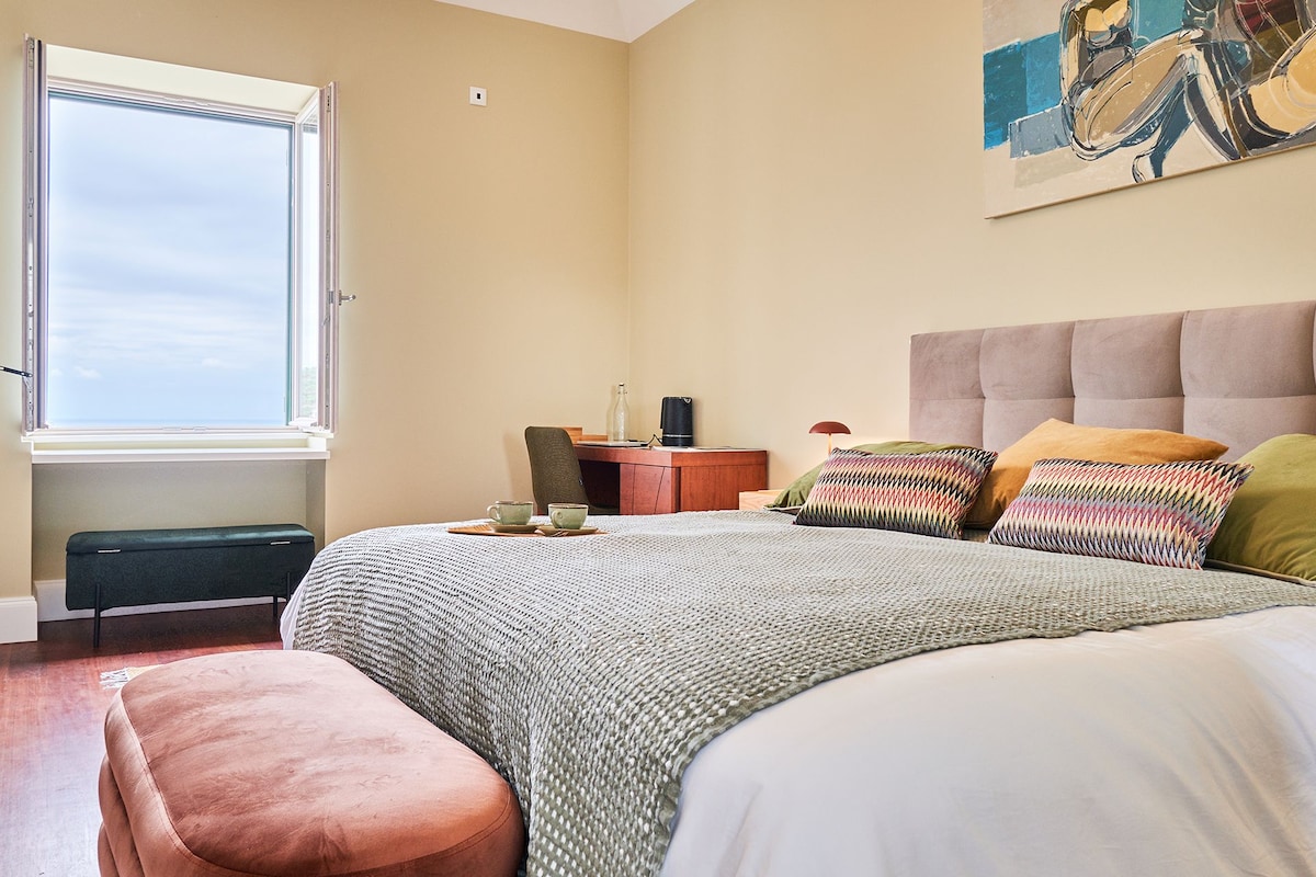 A bedroom with a bed, a bench, a desk, and a window.