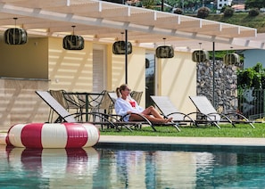 A poolside area with lounge chairs, a pool, and a stone wall. - Quinta do Serrado (Câmara de Lobos)