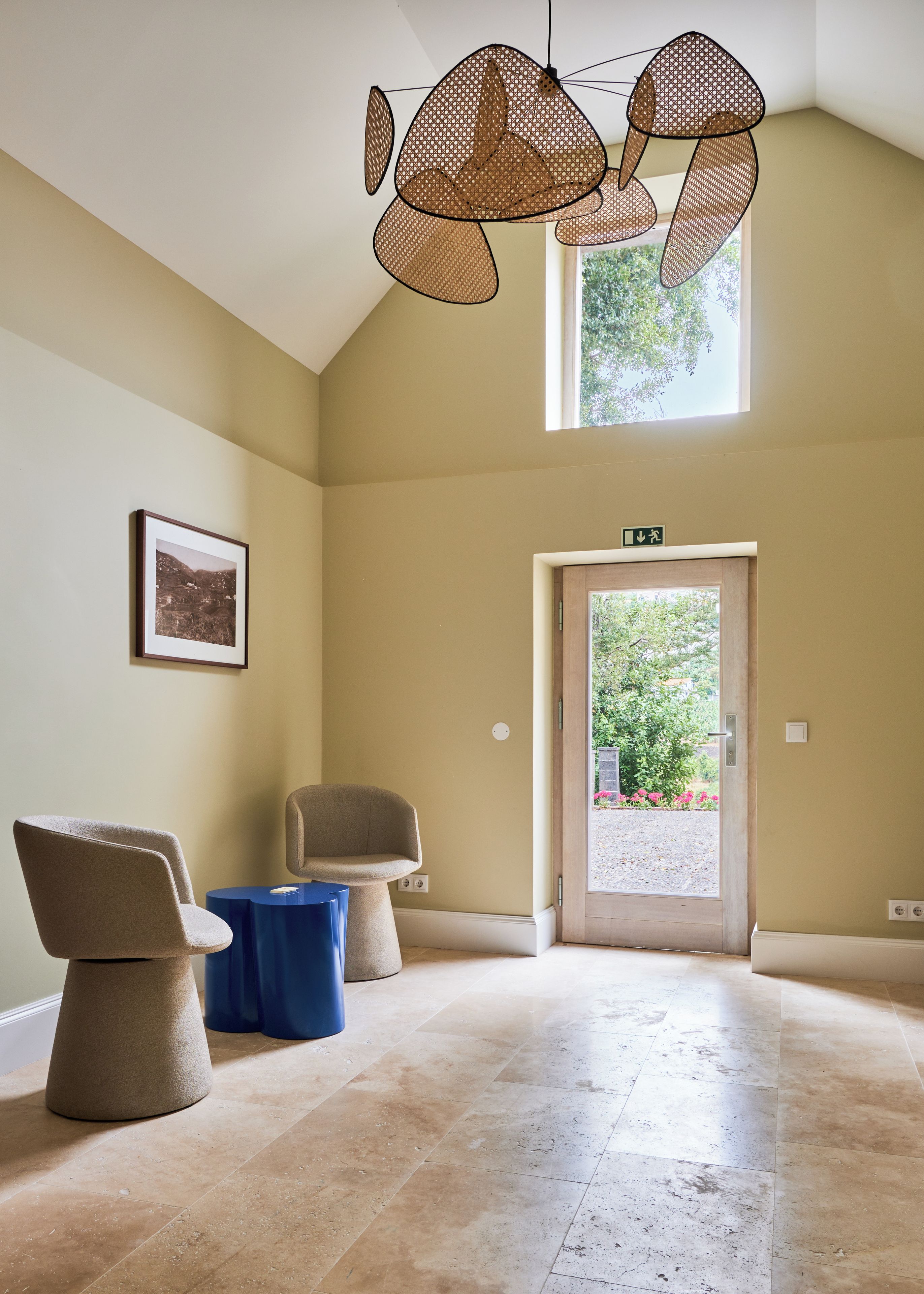 A spacious room with a high ceiling, a door leading outside, and two chairs.