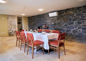 A dining area with a stone wall, a white tablecloth, and red chairs. - Quinta do Serrado (Câmara de Lobos)
