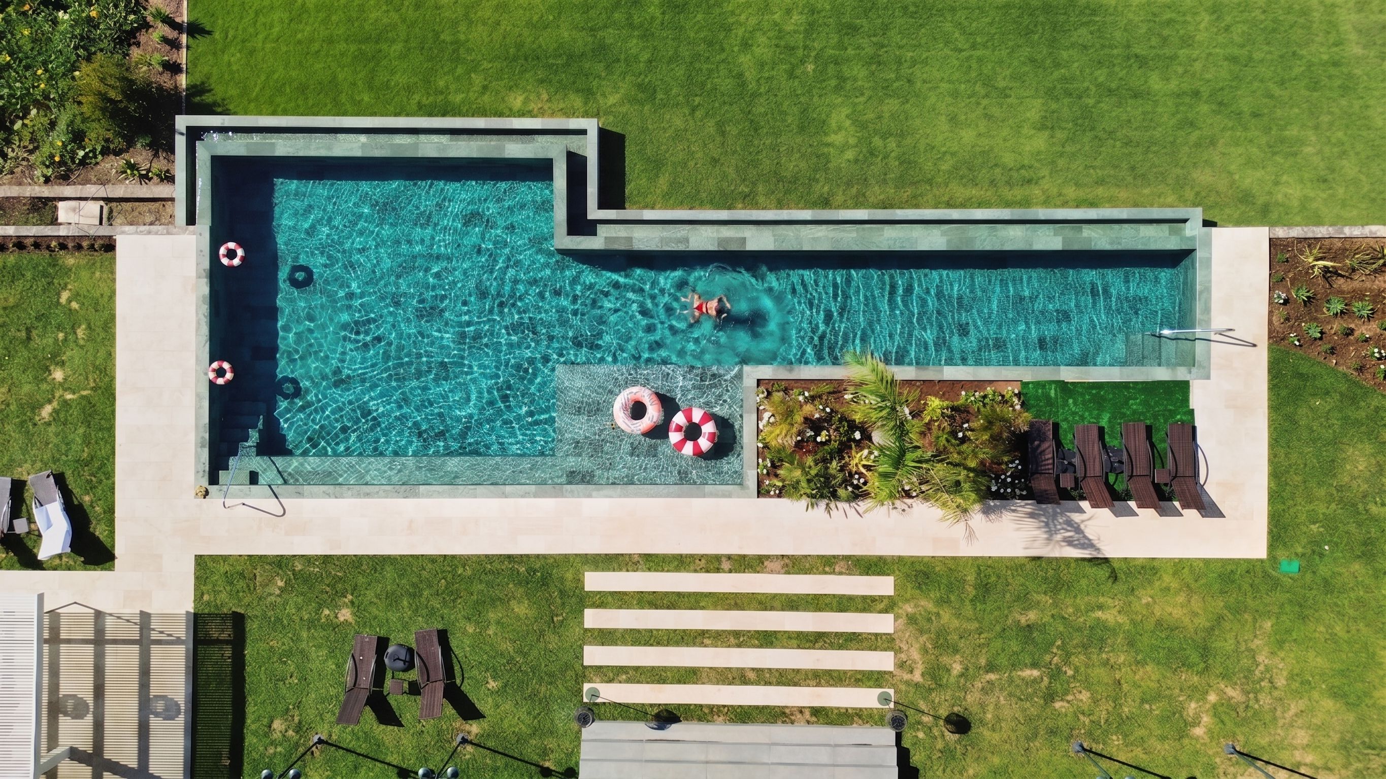 Ein Luftbild eines Schwimmbeckens mit zwei Rettungsringen, einem kleinen Garten mit Pflanzen und einer Sitzgelegenheit mit Stühlen.