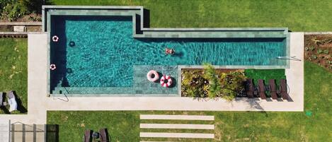 Vista aérea de uma piscina com dois boias, uma pequena área de jardim com plantas e um espaço de estar com cadeiras.