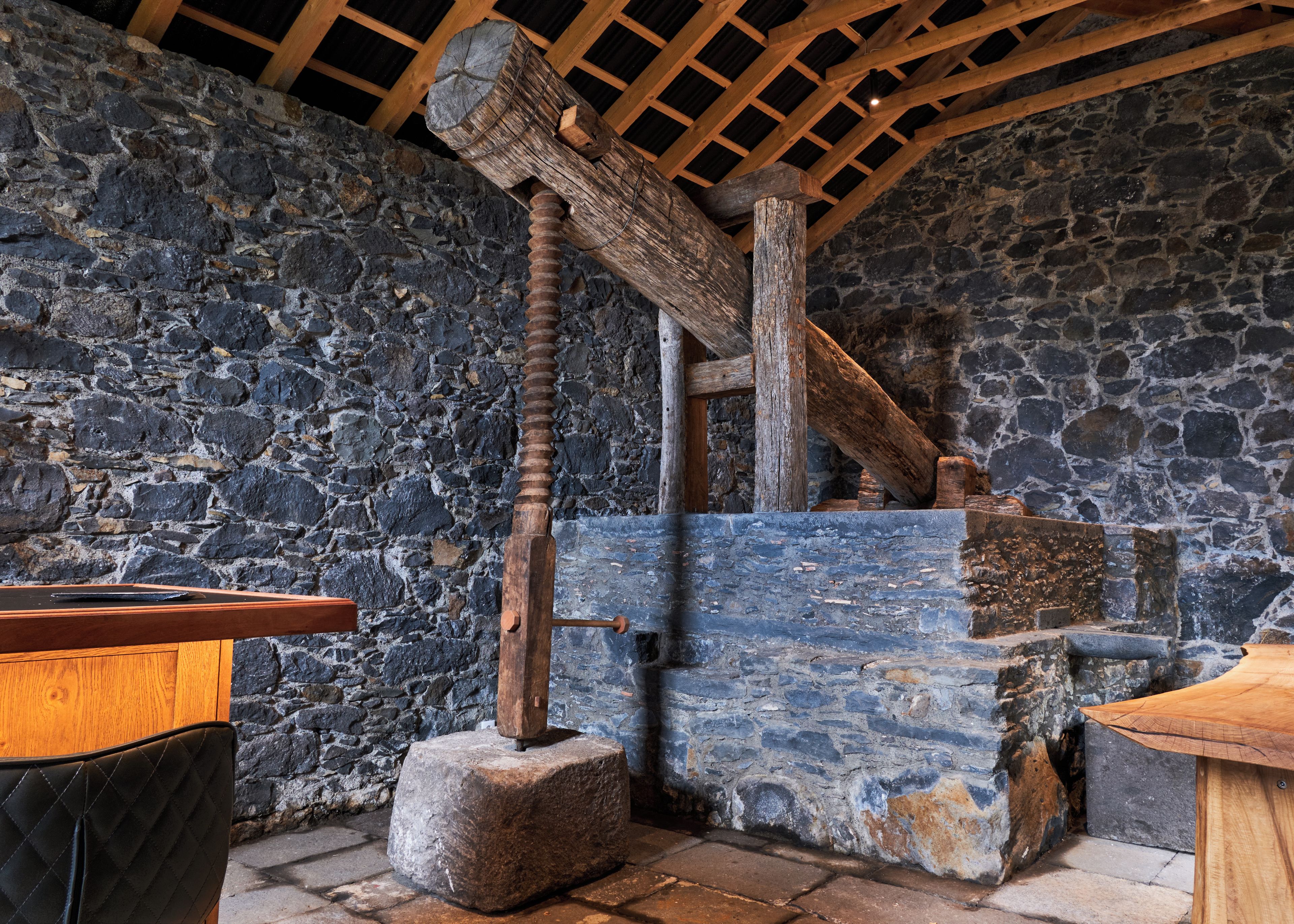 A rustic interior with stone walls, wooden beams, and a stone mill.