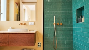 Een badkamer met een witte wastafel, een spiegel, een douchegedeelte betegeld met groen en een houten wastafelmeubel.