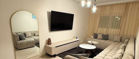 Una sala de estar moderna con un televisor de pantalla plana, un sofá, una mesa de centro y un espejo.
