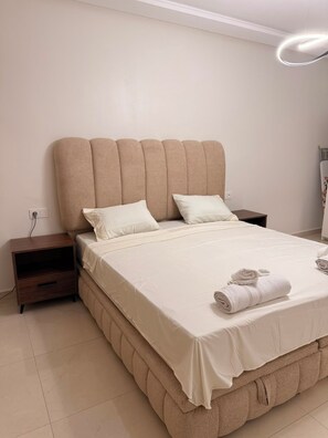 A bedroom with a bed, two pillows, a nightstand, and a wall-mounted light fixture. - Beautiful Family Apartment in the Heart of Nador (Nador)