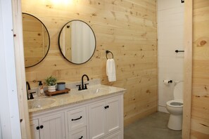 Et badeværelse med træpaneler, en hvid vask med marmorbordplade, et spejl, en bøjle til håndklæder og et toilet.