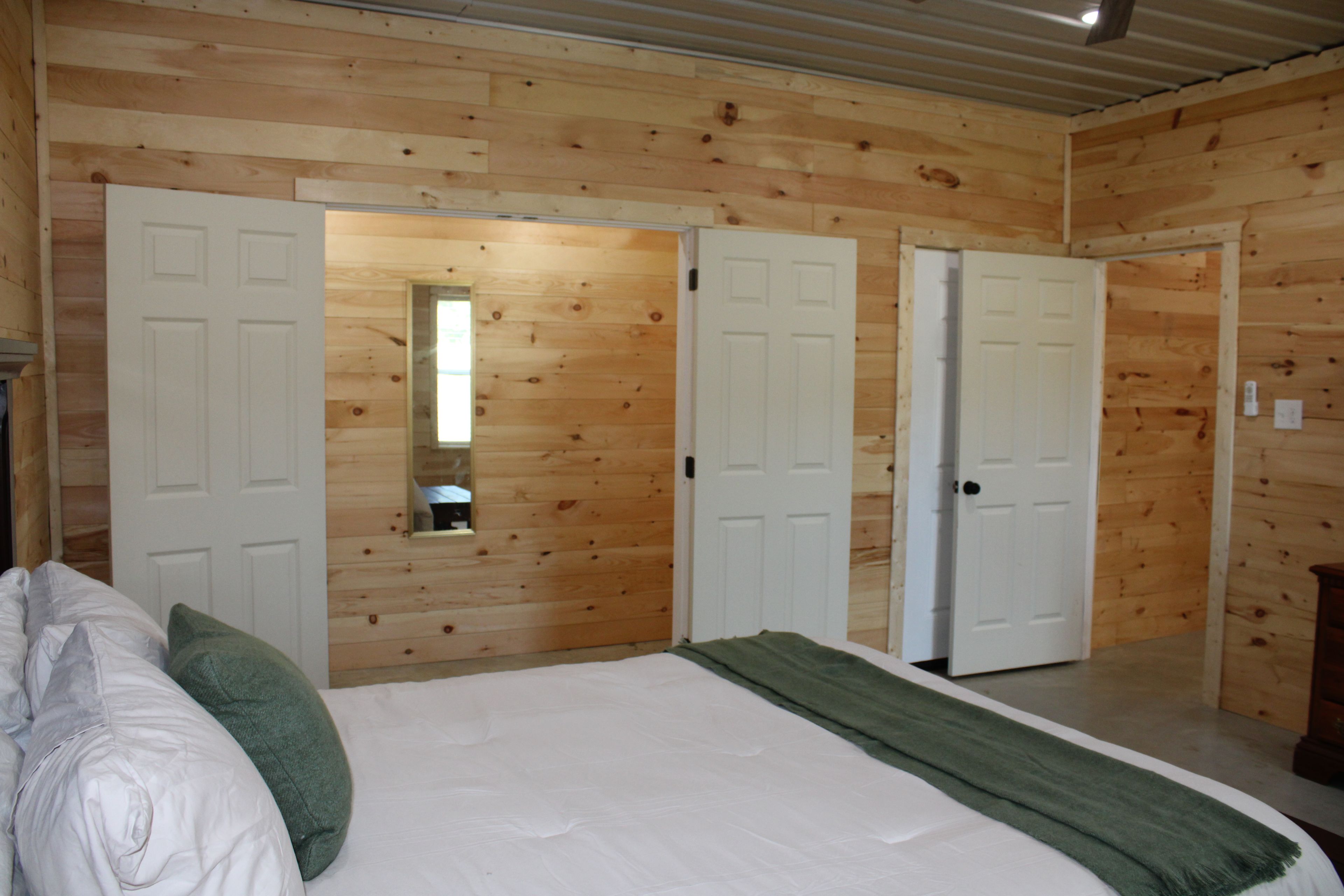 A bedroom with a bed, pillows, a green throw, and wooden walls.