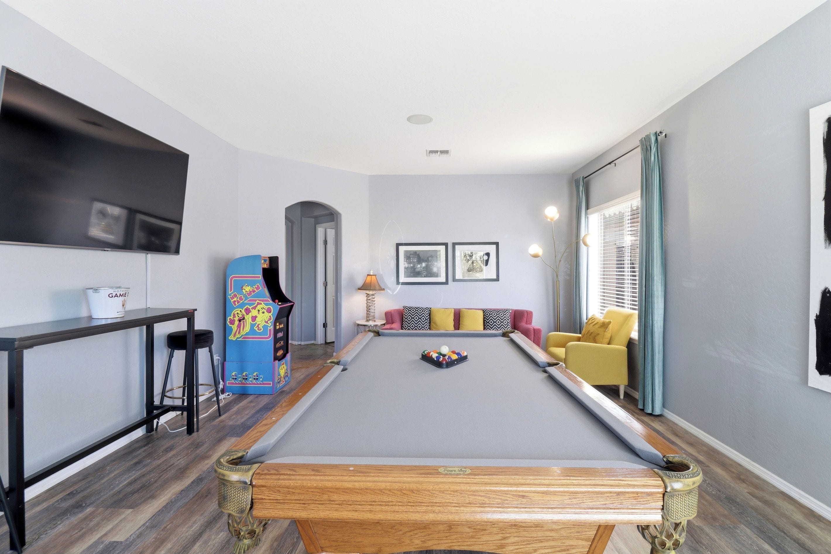 A pool table in a room with a sofa, a TV, and a lamp.