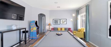 A pool table in a room with a sofa, a TV, and a lamp.
