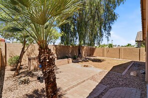 A patio area with a palm tree, a weeping willow, and a brick wall. - 3BR| Near State Farm Stadium| Billiards|Pool Acces (Glendale)