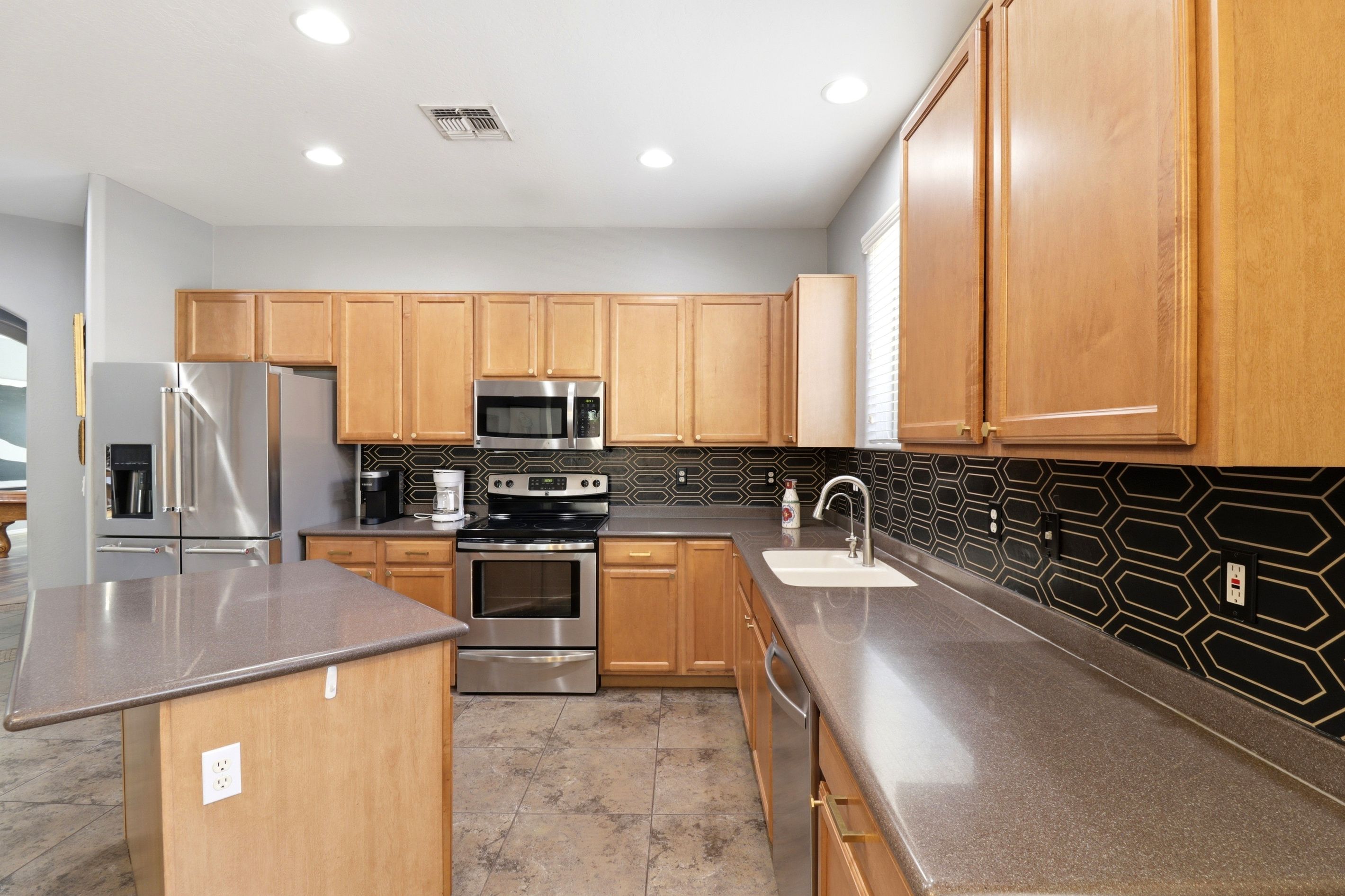 A modern kitchen with wooden cabinets, stainless steel appliances, a black backsplash, and a granite countertop.