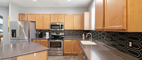 A modern kitchen with wooden cabinets, stainless steel appliances, a black backsplash, and a granite countertop.