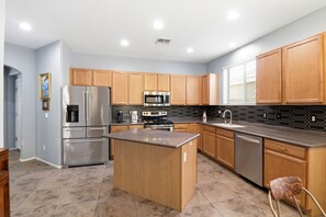 A modern kitchen with stainless steel appliances, wooden cabinets, and a central island. - 3BR| Near State Farm Stadium| Billiards|Pool Acces (Glendale)